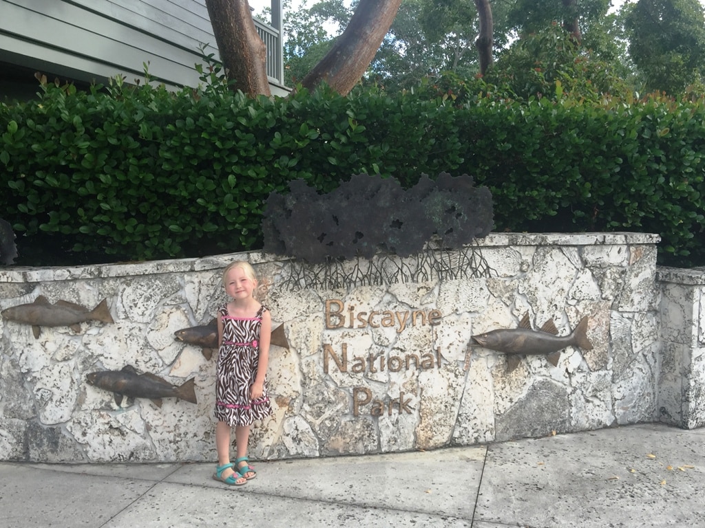 Girl Standing By Biscayne National Park Sign Warmest National Parks To Visit In Winter